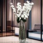 Yellow artificial cherry blossom branches in a glass vase on a wooden table for home decoration.