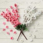 pink and white artificial cherry blossom branches in a glass vase on a wooden table for home decoration.