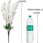 Yellow artificial cherry blossom branches in a glass vase on a wooden table for home decoration.