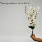 White artificial cherry blossom branches in a glass vase on a wooden table for home decoration.