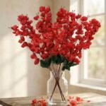 Artificial cherry blossom flowers in red displayed in a clear glass vase for interior decoration.